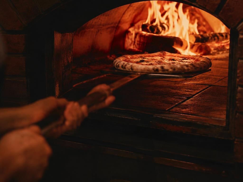 A pizza on a peel sliding into a glowing oven with bright flames